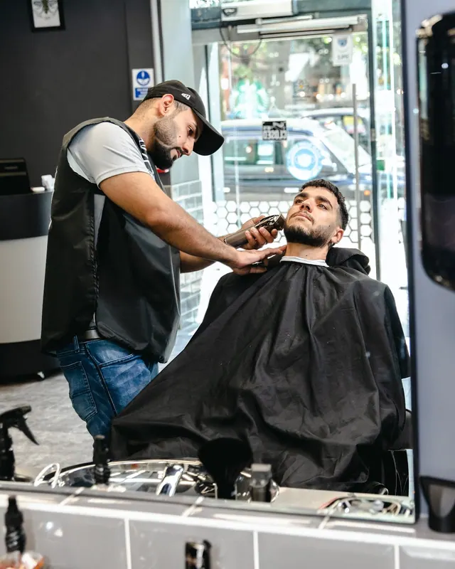 A barber trimming a client’s beard at his station