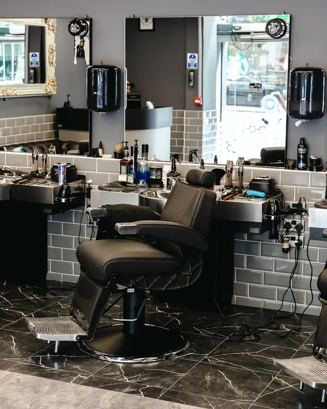 A barber’s station: black leather chair, mirror and grey brick tiles