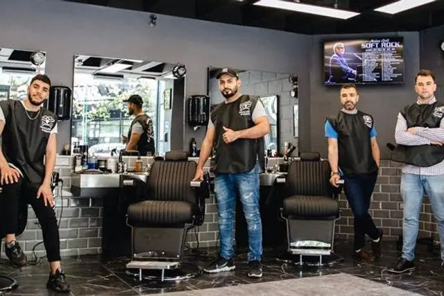 Five barbers standing among the chairs inside the shop