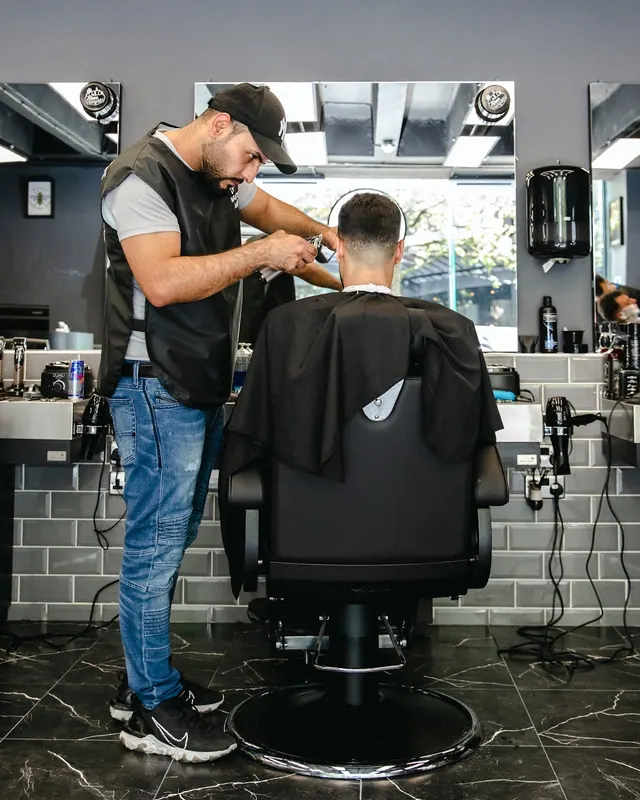 A barber cutting a client’s hair at a station by the window
